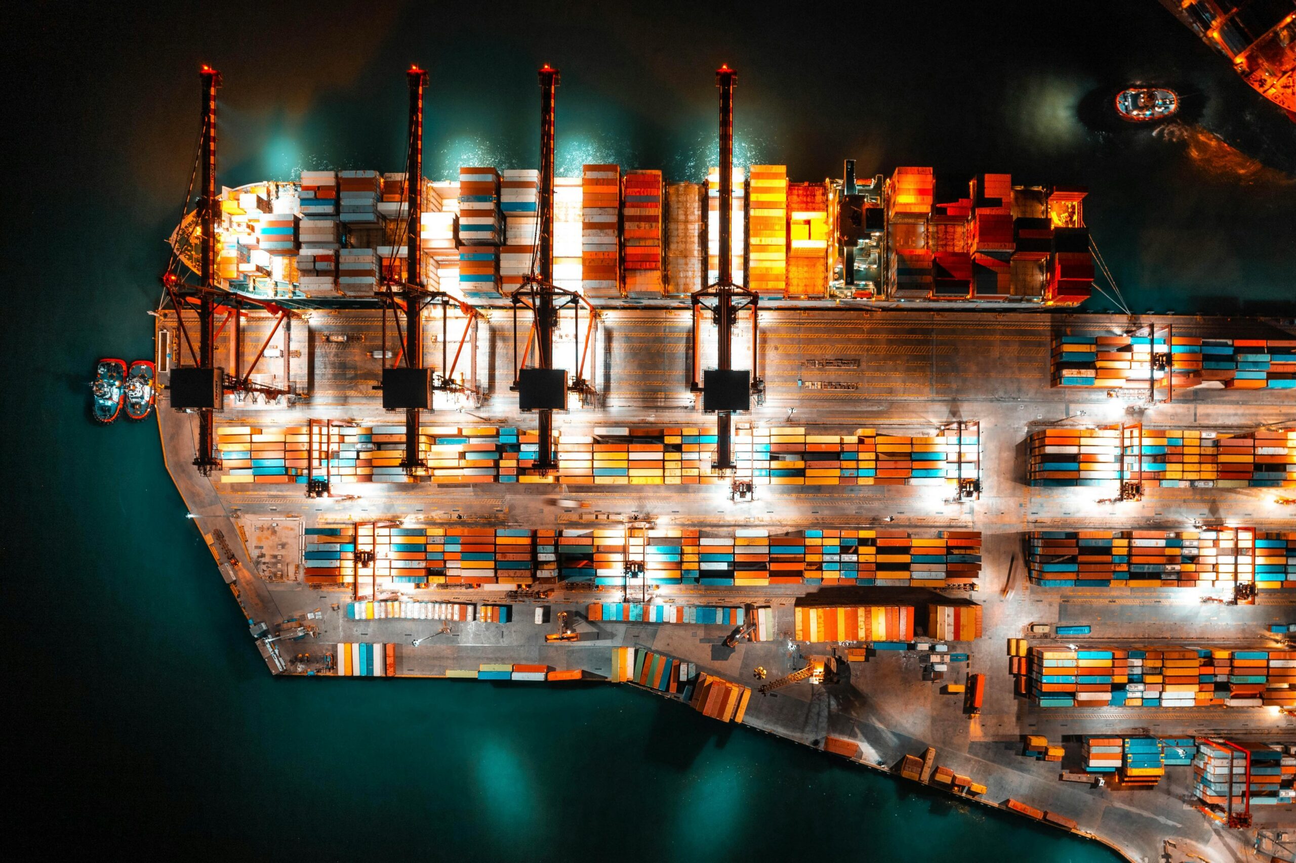 Widok morskiego portu towarowego w nocy. Oświetlone żurawie pracują nad kolorowymi kontenerami.